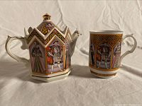 Front view of the teapot and matching cup with color portraits of Henry VIII and his six wives surrounded by patterned details in gold and purple.