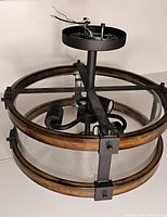 Close-up image showing the circular clear glass shade with two wood rings and black metal frame of the ceiling light fixture. Wiring and mounting hardware are visible on top.