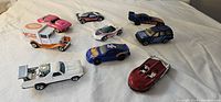 View of all 10 toy cars arranged on a white fabric surface showing variety of styles and colors including race cars, convertibles, trucks.