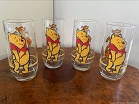 Set of four clear glasses with vintage Disney Winnie the Pooh and Tigger artwork, arranged on wooden surface.