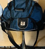 Photo of one large blue and black duffel bag showing the front with panda logo patch, black adjustable shoulder strap, multiple zippered compartments with white piping.