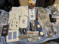 Photo of assorted outlet covers, switch plates, and dimmer switches in plastic packaging and loose, laid out on table.
