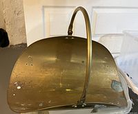 Brass log holder curved scoop with handle, showing patina and wear marks.