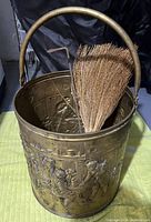 Photo showing embossed brass coal bucket with rounded handle and a natural fiber brush inside.