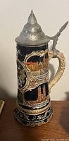 Side view of the European musical stein showing intricate colorful illustrations, pewter lid with finial, and textured handle.