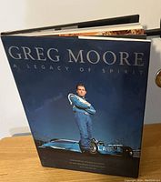 Photo showing the front cover of the hardcover book 'Greg Moore: A Legacy of Spirit' with a man in racing suit and race car.