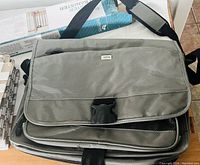 Front and part of the side view showing gray fabric laptop bag with brand Solo logo, adjustable shoulder strap with padding, front flap with clip buckle.
