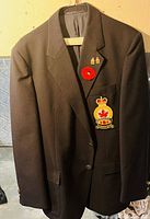 Front view of dark brown Legion jacket with embroidered emblem patch, two metal pins, and red poppy pin on left side lapel.