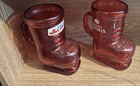 Two reddish-brown glass mugs shaped like boots with Molson Canadian logos, placed on wooden surface.