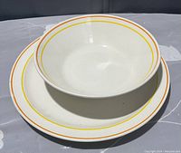 Photo showing the bowl placed on top of the plate, both cream colored with orange rings near rim.