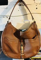 Front view of the brown leather Nine West purse showing the shoulder strap, front pocket, and gold-tone buckle clasp.