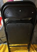 Photo showing the back and folded seat of two black metal folding chairs stacked together