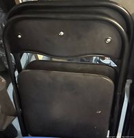 Back view of two black metal folding chairs stacked together showing the folding mechanism and metal frame.