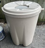 Beige plastic rain barrel with lid featuring central circular mesh opening, minor wear visible, condition unknown due to crack. Includes side spout.