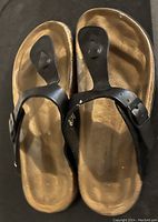 Top down photo of a pair of size 8 ladies sandals with black leather straps and buckles, tan footbed showing light wear.