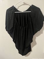 Front view of a black sequin blouse hanging on a white hanger showing loose fit, scoop neckline, and wide sleeves with sequin detailing.