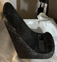 Side angle showing the curved shape and slot at the base of the black speckled stone cell phone holder