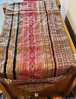 Photo showing full length of table runner with detailed multicolored woven patterns in gold, red, blue, and brown.