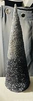 Photo of a silver tabletop Christmas tree made entirely of densely applied sequins, forming a textured shiny surface with a pointed cone shape.