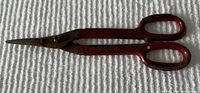 Photo of one pair of vintage sewing shears with rusty metal blades and red painted handles on a white textured surface.
