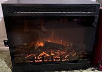 Front view of the black electric fireplace insert showing the realistic flame effect and logs inside the glass front panel.