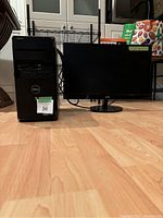 Side by side of black Dell desktop tower and 24-inch black AOC monitor on hardwood floor