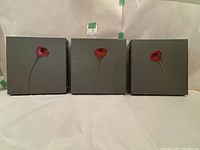 Front view of three square gray panels each with a single red poppy flower in the center.
