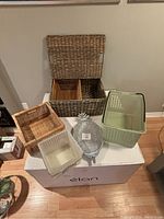 Overview of all six assorted storage baskets displayed on a white box against a wall, showing various sizes, shapes and materials.