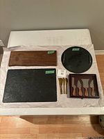 Overview of all cheese boards and cheese serving accessories on table including wooden, slate, and ceramic boards with spreader knives and boxed cheese knives.