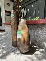 Two decorative vases side by side on outdoor pavement with wooden and stone background, showing detailed textures and shape differences.