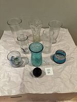 Nine assorted vases of various glass types, sizes, colors and shapes, arranged on white background.