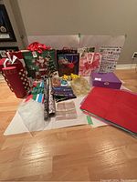 Overview of all gift bags, wrapping paper rolls, and tissue paper included in the lot placed on a white background on floor.