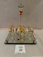 Photo showing the decanter with stopper centered on the mirrored tray, surrounded by five matching glasses with gold and orange floral decoration.