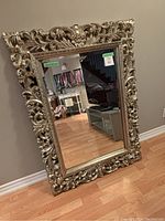 Full view of the gold filigree mirror standing against a wall, showing the entire rectangular mirror with its detailed ornamental frame.
