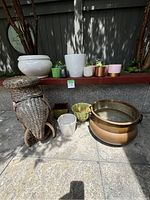 Overall view of all plant pots and wicker elephant plant stand arranged on ground and bench, showing variety in sizes and materials.