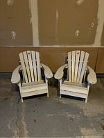 Photo shows two white wooden kids' Muskoka chairs side by side in a garage setting, clearly showing their size, shape, and weathered condition.
