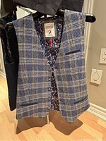 Front view of a blue and white checkered men's vest with buttons and floral lining shown hanging