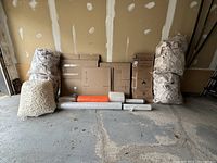 Overview of all moving supplies neatly arranged in garage, showing boxes, bags of packing paper, packing peanuts, and rolls of stretch wrap and bubble wrap.
