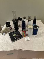 Full lot showing the Ninja blender with blending cups, assorted portable water bottles, coffee tumblers, and recipe book arranged on a white surface.