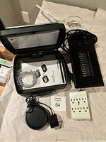 Photo showing the open SentrySafe portable safe with keypad, instruction manual, cables inside, black Cyclone Booster fan, black Amazon Alexa Dot with cord, and a white power strip.