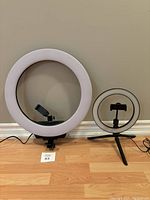 Two ring lights side-by-side on the floor and against wall, showing size difference and phone holders.