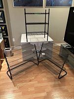 Photo showing one black metal shoe rack with three wire shelves placed on a white platform, along with two grey mesh shoe racks placed on the floor in front of it.