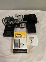 Sony Cybershot digital camera and all included accessories laid out: Sony battery charger, ProMaster XtraPower Traveler rapid battery charger in box, soft carrying case, camera with lens extended, power cords.