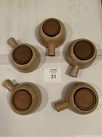 Five stoneware soup bowls shown from bottom side, beige exterior with rustic finish and handles.