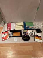 Full lot display on wooden floor with stationery items including pencils, notebooks, cardstock paper, portfolios, puzzle letter kits, glue stick, and felt cat pouch