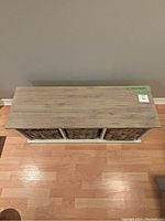 Top view of storage bench showing wood grain top and three wicker baskets inside frame