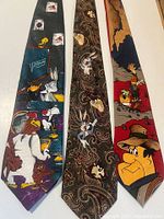 Three vintage silk Looney Tunes ties laid flat showing full design of Bugs Bunny, Fred Flintstone, Tasmanian Devil and other characters.