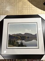 Full view of framed print of Smoke Lake by A.J. Casson showing black wood frame and white double mat against floor background