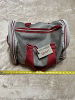 Front and top view of the gray and red Dolce & Gabbana sport duffel bag with attached brand tag and handles visible, laid on a beige carpet with a measuring tape showing approximate dimensions.