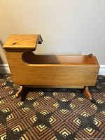 Side view of the pine baby rocker showing its smooth wooden finish and curved rockers on a patterned carpet.
